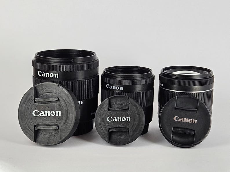 May include: Three black Canon camera lenses with lens caps. The lenses are all different sizes and have the Canon logo on them.
