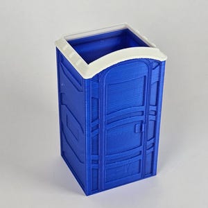 May include: A blue plastic portable toilet model with a white roof and a door. The toilet is a miniature version of a real portable toilet.