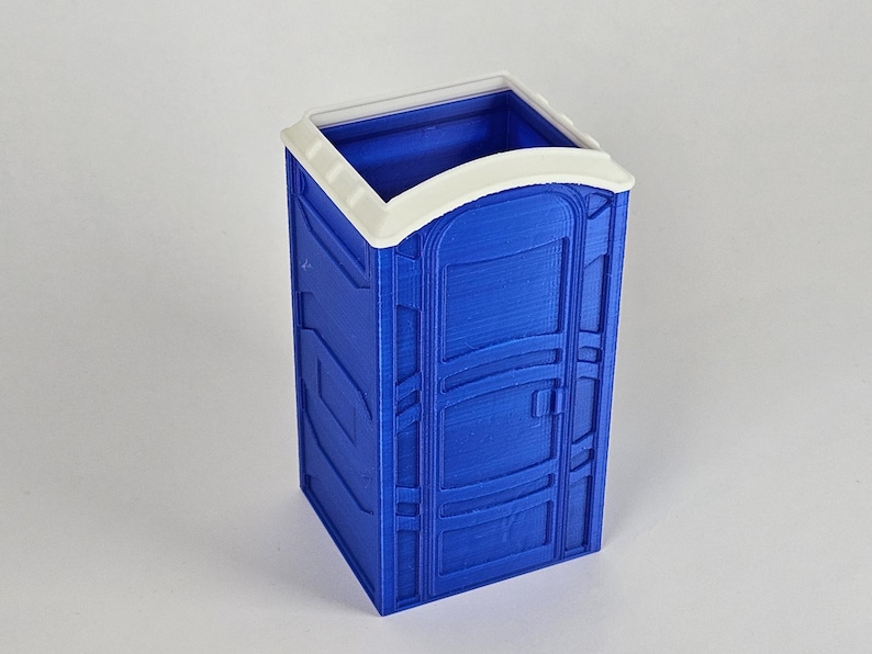 May include: A blue plastic portable toilet model with a white roof and a door. The toilet is a miniature version of a real portable toilet.