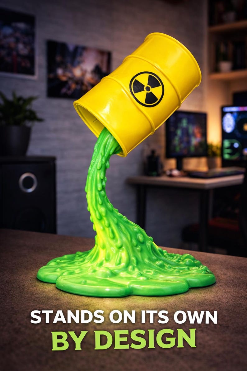 May include: A yellow barrel with a black radiation symbol is tilted, pouring out a stream of bright green, textured liquid. The liquid pools at the base, forming a unique decorative piece. Text reads: STANDS ON ITS OWN BY DESIGN.