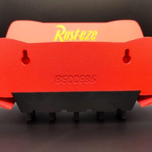 May include: Red and black wall-mounted shelf with the word "Rusteze" in yellow. The shelf has two keyhole slots for hanging and the number "86C0E86" printed on the front. The shelf has a black base with several small, rectangular supports.