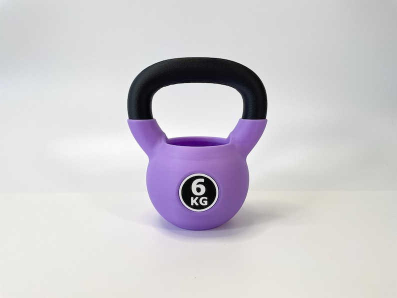 May include: A purple kettlebell with a black handle. The weight is indicated as 6 KG on a white and black circular sticker. This fitness equipment is designed for strength training and exercise routines.