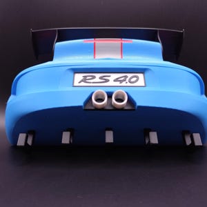 K&ouml;nnte beinhalten: Heck eines blauen Spielzeugautos mit einem schwarzen Spoiler. Das Auto hat ein wei&szlig;es Nummernschild mit der Aufschrift "RS 4.0". Es hat zwei wei&szlig;e Auspuffrohre und mehrere graue rechteckige Details. Ein roter Streifen akzentuiert die Oberseite.