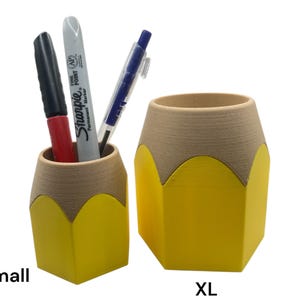 May include: Two yellow pencil-shaped desk organizers, one labeled "Small" and the other labeled "XL". The smaller organizer has two pens inside, one red and one black.