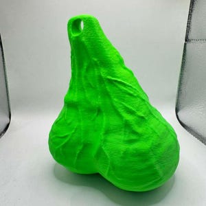 May include: A bright neon green, three-dimensional object with a textured, organic surface featuring prominent vein-like ridges and a rounded, dual-lobed base. The top section tapers to a point and includes a circular hole for hanging or attachment.