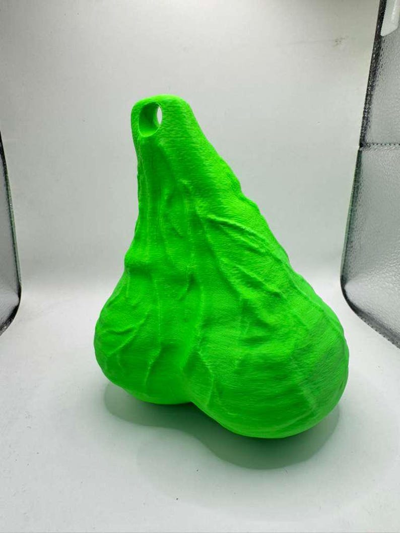 May include: A bright neon green, three-dimensional object with a textured, organic surface featuring prominent vein-like ridges and a rounded, dual-lobed base. The top section tapers to a point and includes a circular hole for hanging or attachment.