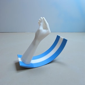 Op de afbeelding: Een sculptuur van een witte arm en hand met een gebogen basis met blauw-witte strepen. De hand is in een gebaar en de basis is een gestileerd ontwerp.