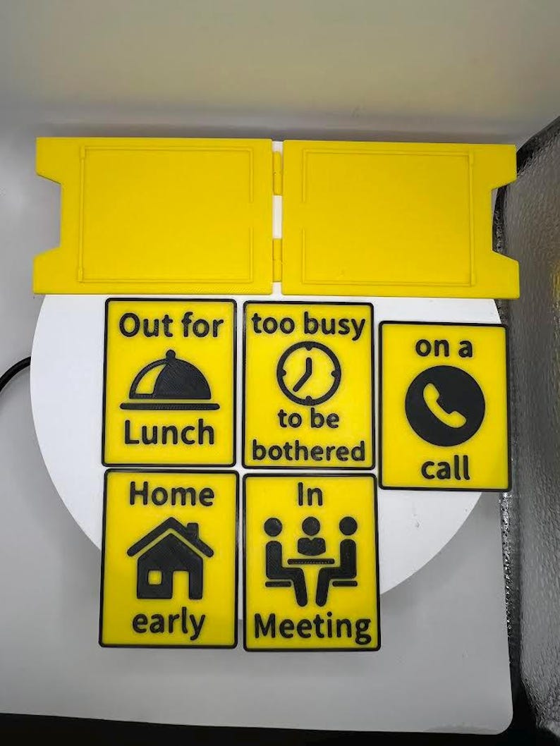 May include: Yellow and black signs with various messages, including "Out for Lunch," "Too busy to be bothered," and "On a call." Other signs read "Home early" and "In Meeting." The signs are designed to be easily visible.
