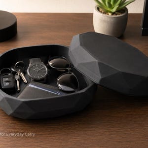 Puede incluir: Una bandeja negra de forma geom&eacute;trica con tapa a juego, que contiene un reloj, gafas de sol, llaves y una cartera. La bandeja est&aacute; abierta, revelando su contenido. El texto "Perfect for Everyday Carry" es visible en la parte inferior de la imagen.