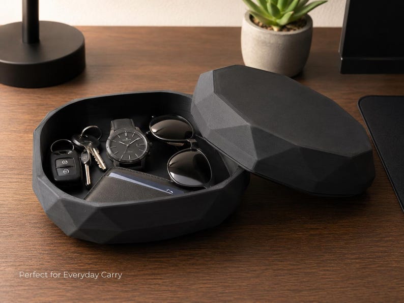Puede incluir: Una bandeja negra de forma geom&eacute;trica con tapa a juego, que contiene un reloj, gafas de sol, llaves y una cartera. La bandeja est&aacute; abierta, revelando su contenido. El texto "Perfect for Everyday Carry" es visible en la parte inferior de la imagen.