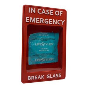 May include: A red emergency box with the words "IN CASE OF EMERGENCY" and "BREAK GLASS" in white. Inside the box is a blue and white Lifestyles condom package. The package reads "TOUGH/RESISTANT".