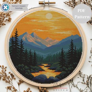 May include: A completed cross-stitch landscape scene in a wooden embroidery hoop. The design features a mountain range, river, and forest under a sunset sky. The text "Pattern Keeper TESTED" and "PDF Pattern" are visible.