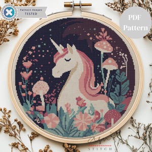 Puede incluir: Patrón de punto de cruz con un unicornio con melena y cuerno rosas, rodeado de flores y setas. El diseño está en un bastidor de bordado de madera. El texto "PDF Pattern" es visible.