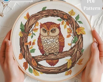 May include: Cross-stitch pattern featuring a detailed owl perched on a branch, surrounded by a wreath of autumn leaves. The owl has brown and orange feathers. The text "PDF Pattern" is visible. The text "Pattern Keeper Tested" is also visible.