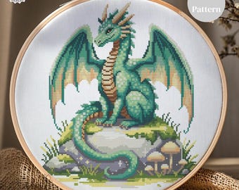 Può includere: Un modello a punto croce di un drago verde con ali e squame dettagliate, appollaiato su una roccia muschiosa. Il disegno è incorniciato in un telaio da ricamo in legno. I testi "Pattern Keeper TESTED" e "PDF Pattern" sono visibili.