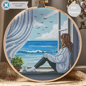 Puede incluir: Bordado de punto de cruz en un aro de madera que representa una serena vista del océano a través de una ventana. Una persona está sentada en el alféizar, mirando el mar y el cielo azules. El texto "Pattern Keeper TESTED" y "PDF Pattern" son visibles.