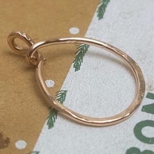May include: A rose gold pendant with a hammered texture. The pendant has a teardrop shape with a small loop at the top for a chain. The metal has a warm, reflective sheen.