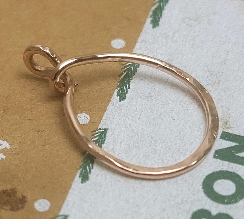 May include: A rose gold pendant with a hammered texture. The pendant has a teardrop shape with a small loop at the top for a chain. The metal has a warm, reflective sheen.