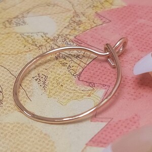 May include: A rose gold-colored ring with a delicate, oval design. The ring features a knot detail at the top, adding a unique touch. The ring is displayed on a map-themed background, showcasing its elegant simplicity.