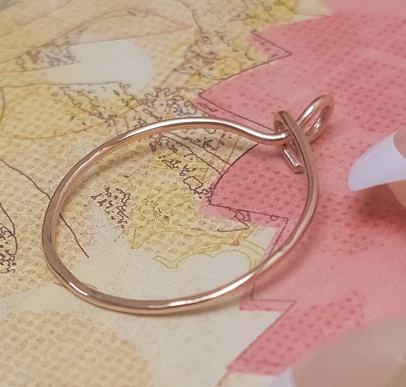 May include: A rose gold-colored ring with a delicate, oval design. The ring features a knot detail at the top, adding a unique touch. The ring is displayed on a map-themed background, showcasing its elegant simplicity.
