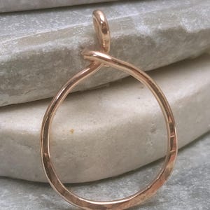 May include: A handcrafted, rose gold-colored pendant with a teardrop shape. The pendant is made of a single piece of wire, looped into a circle with a small loop at the top for a chain. The surface has a hammered texture.