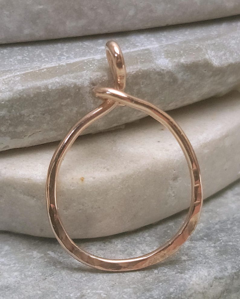May include: A handcrafted, rose gold-colored pendant with a teardrop shape. The pendant is made of a single piece of wire, looped into a circle with a small loop at the top for a chain. The surface has a hammered texture.