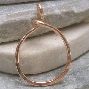 May include: A hammered-finish, rose gold pendant with a teardrop shape. The pendant is a continuous loop, with a small loop at the top for a chain. The metal has a warm, reflective quality.