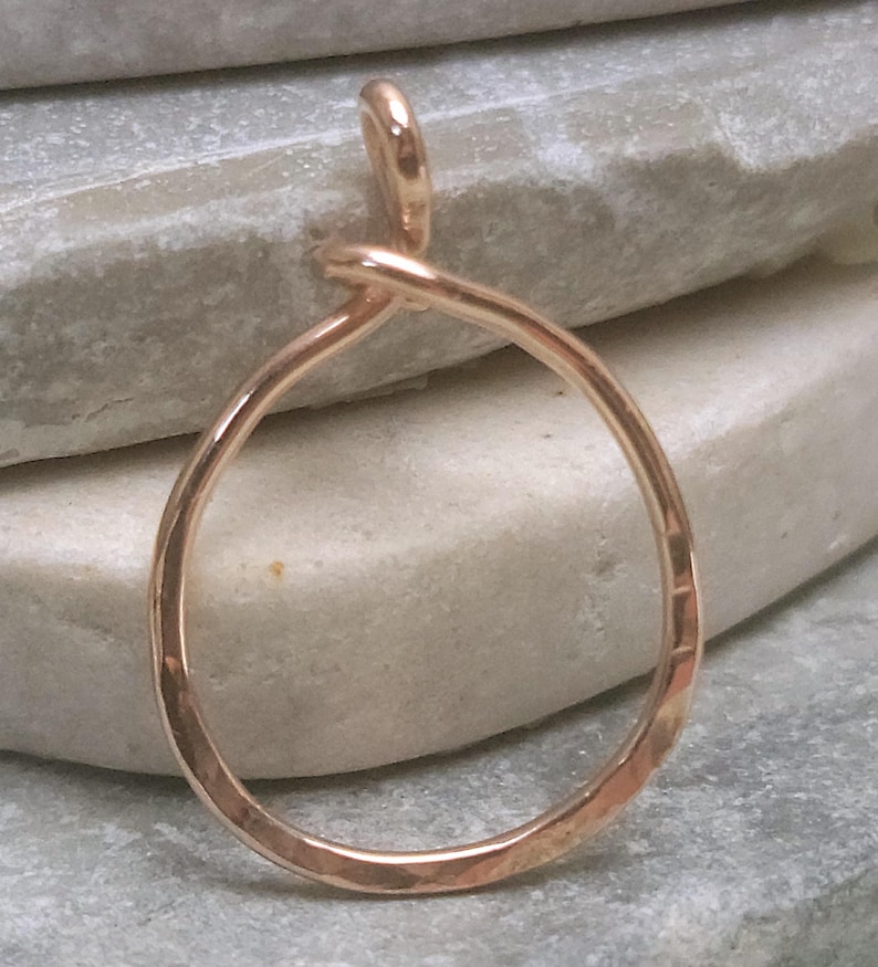 May include: A hammered-finish, rose gold pendant with a teardrop shape. The pendant is a continuous loop, with a small loop at the top for a chain. The metal has a warm, reflective quality.