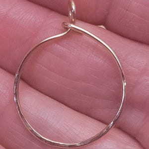 May include: A gold-colored, hammered metal hoop earring with a small loop at the top for hanging. The earring is a simple, minimalist design, perfect for everyday wear. The hoop is approximately 1 inch in diameter.