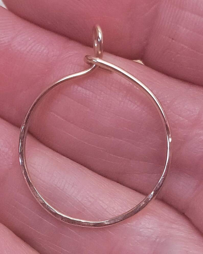 May include: A gold-colored, hammered metal hoop earring with a small loop at the top for hanging. The earring is a simple, minimalist design, perfect for everyday wear. The hoop is approximately 1 inch in diameter.