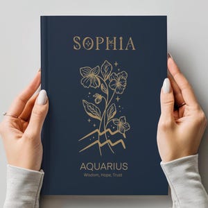 May include: A dark blue hardcover journal featuring gold foil lettering and line art. The cover displays the name SOPHIA at the top, a floral illustration with the Aquarius zodiac symbol below it, and the text AQUARIUS Wisdom, Hope, Trust.
