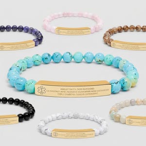 May include: Assortment of beaded bracelets in various colors, including blue, pink, and black. Each bracelet features a gold-colored rectangular plate with medical information and an emergency symbol. The bracelets are designed for medical identification.