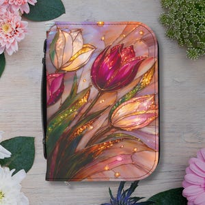 May include: A zippered wallet featuring a stained-glass style tulip design in shades of pink, purple, and gold. The wallet has a black border and a black zipper. The floral design includes green leaves and a light background.