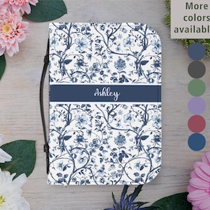 Op de afbeelding: Een bloemenpatroon boekcover in wit en marineblauw. Het ontwerp heeft een herhalend patroon van bloemen en wijnranken. Een marineblauwe band over het midden toont de naam "Ashley" in cursief. De cover heeft een zwarte band en is omgeven door bloemen.