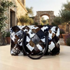 May include: A rectangular handbag featuring a patchwork design of cowhide in shades of brown, black, and white. The bag has two dark brown leather handles attached to the top and a structured shape with a diamond-patterned exterior surface.