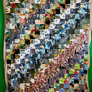 May include: A large patchwork quilt made of many different colorful fabrics with tropical prints. The quilt is made up of squares of fabric, each with a different design. The quilt is a vibrant and colorful piece of art.