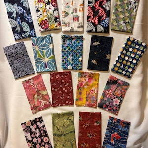 May include: A collection of seventeen rectangular fabric tissue holders featuring various patterns including koi fish, floral motifs, geometric shapes, cranes, and animal prints in a wide array of colors such as red, blue, green, yellow, and black.