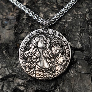 May include: A silver-toned pendant necklace featuring a detailed circular pendant. The pendant depicts a woman with flowing hair and two animals, possibly wolves or cats. The necklace chain is a woven design.