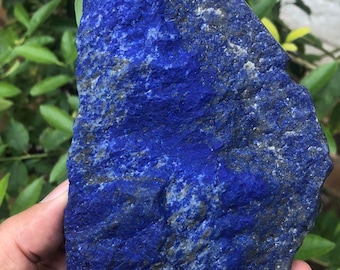 May include: A raw, unpolished piece of lapis lazuli stone featuring a deep, vibrant blue color with visible natural inclusions of gold-colored pyrite and white calcite veins throughout its textured, jagged, and irregular surface.