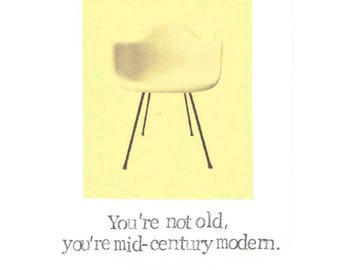 May include: A yellow card with a black and white illustration of a mid-century modern chair. The text on the card reads "You're not old, you're mid-century modern."
