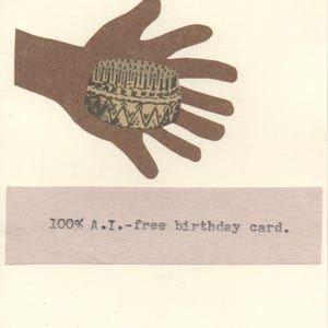 May include: A brown hand holds a detailed illustration of a birthday cake with candles. Below the illustration is a banner with the text "100% A.I.-free birthday card."