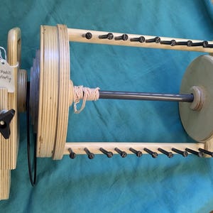 Pode incluir: Um enrola-fio de madeira com um fuso de metal cinza e uma etiqueta que diz "Para a Mãe e Firefly".