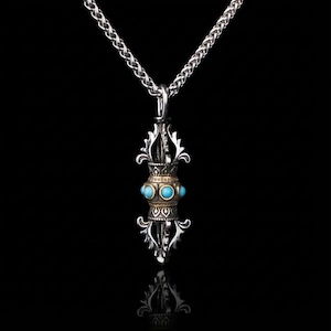 May include: A silver pendant necklace with an ornate pendant, gold detailing, and turquoise-coloured stones. The pendant hangs from a silver chain. The background is black.