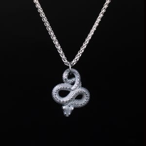 Op de afbeelding: Zilverkleurige slangenhangerketting. De hanger is een gedetailleerd, opgerold slangenontwerp. De ketting heeft een textuur, schakelstijl. De achtergrond is effen zwart, wat de sieraden benadrukt.