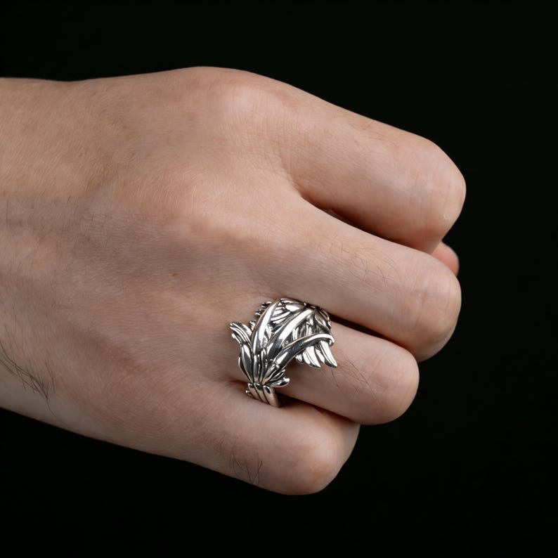 Peut inclure: Une bague en argent avec un motif de feuilles d&eacute;taill&eacute;. La bague pr&eacute;sente plusieurs couches de feuilles, cr&eacute;ant un aspect textur&eacute; et naturaliste. La bague est port&eacute;e sur un doigt sur fond sombre.