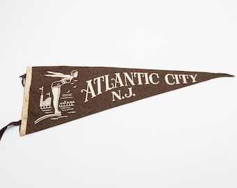 May include: A brown felt pennant with white text and a graphic of a woman diving into water. The text reads "ATLANTIC CITY N.J."