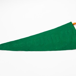May include: A green pennant flag with orange ties. The pennant is a long, triangular shape, made of a felt-like material. The orange ties are at the top of the pennant.