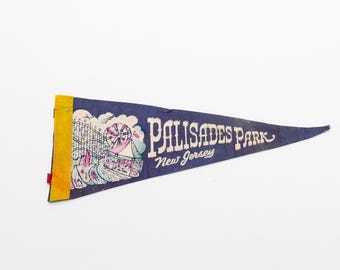 May include: A blue pennant with a yellow border and white text that reads "Palisades Park, New Jersey". The pennant features a colorful illustration of a Ferris wheel and other amusement park attractions.