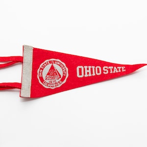 May include: A red felt pennant with white text and a white logo. The text reads "Ohio State". The logo is a circle with the words "Ohio State University" and "Columbus 1870" around a stylized image of a building.