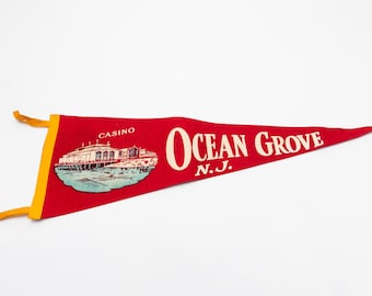 May include: A red pennant with the words "Ocean Grove N.J." in white lettering. The pennant features an illustration of a building labeled "Casino" and has a yellow border and ties.